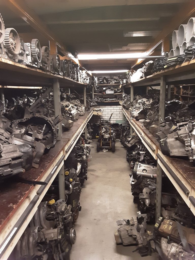Het onderdelenmagazijn: een gang tussen stellingen vol motoren, versnellingsbakken en nokkenassen